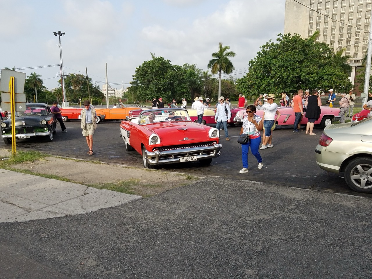 People gathering around brightly colored classic cars on a street in Cuba